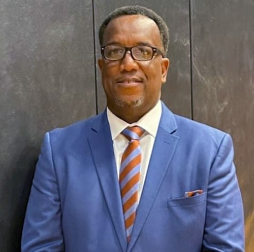 Headshot of a man in glasses wearing a blue suit with blue and orange striped tie