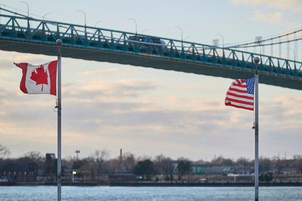 Two flags fly in front of a vehicular bridge