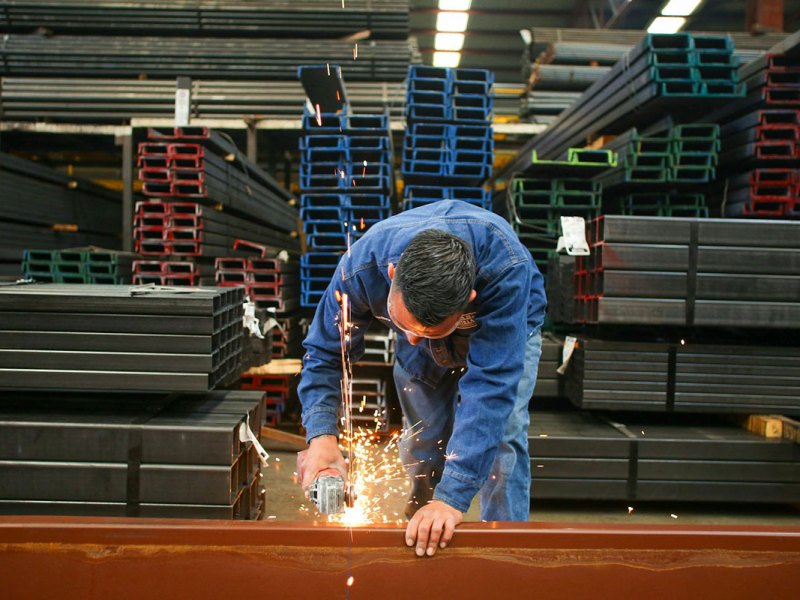 A steel worker cuts a beam in a warehouse full of steel beams
