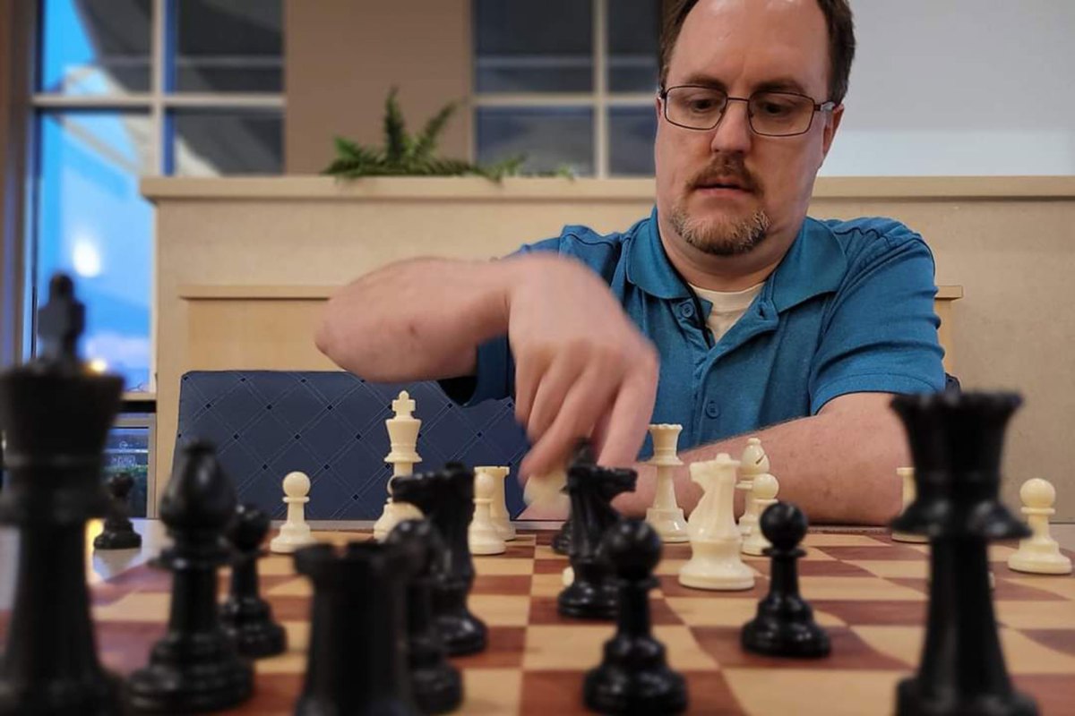 A man in a blue shirt playing chess as seen from the other side of the board