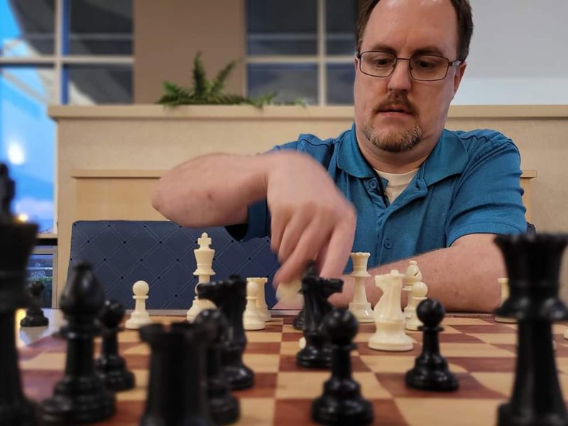 A man in a blue shirt playing chess as seen from the other side of the board