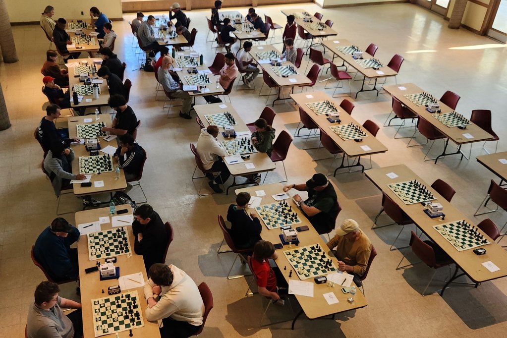 An overhead view of 30 tables set up to play chess, many filled with players