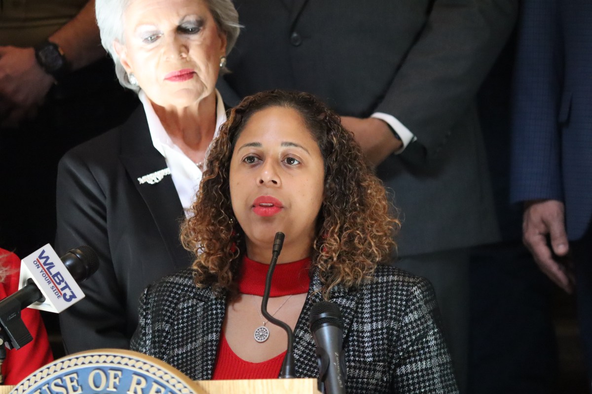 A woman speaks at a podium wearing a black and white print jacket with a red dress under it
