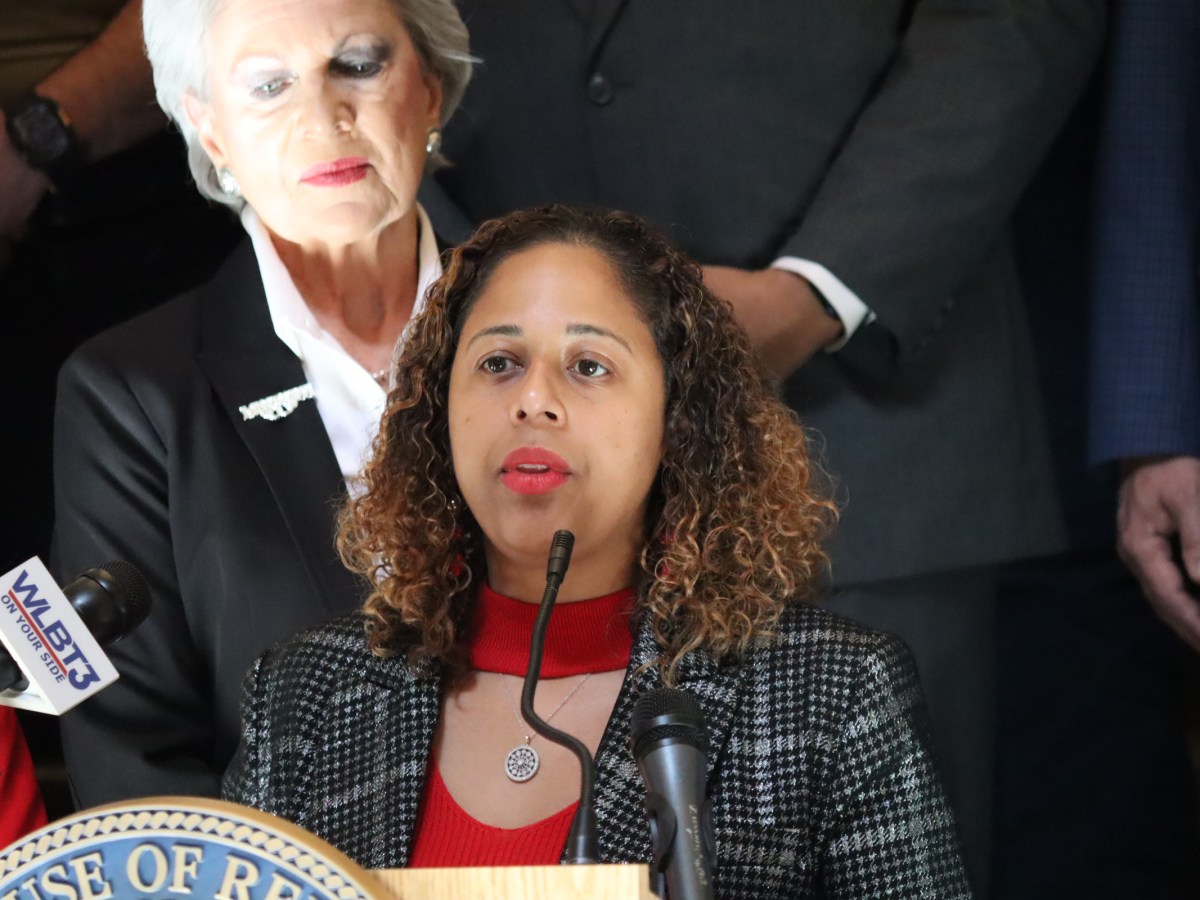 A woman speaks at a podium wearing a black and white print jacket with a red dress under it