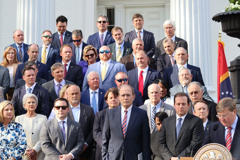 Men and women stand on the steps of a white building with columns