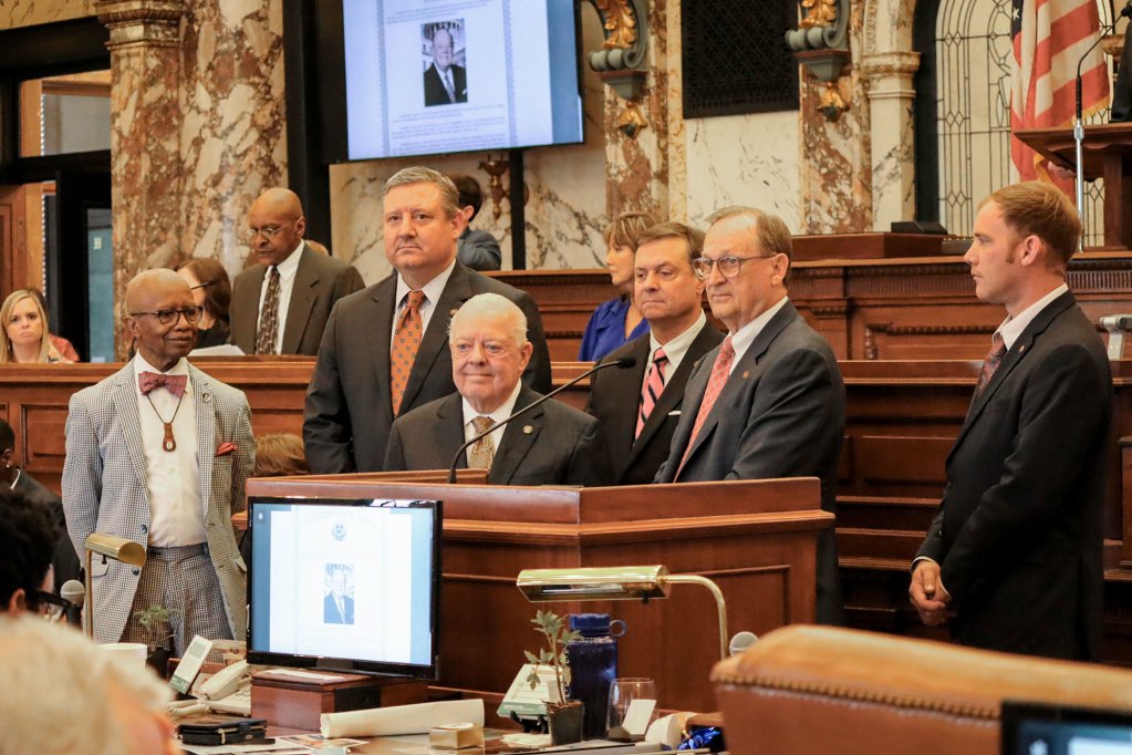 Six men wearing suits stand around a podium.