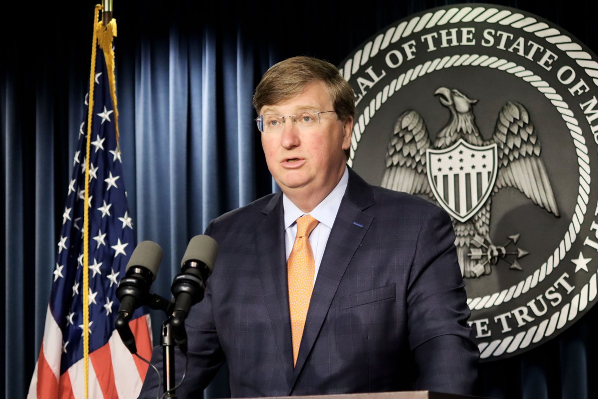 Governor Tate Reeves speaking at a press conference with an American flag next to him and a State of Mississippi official seal behind him