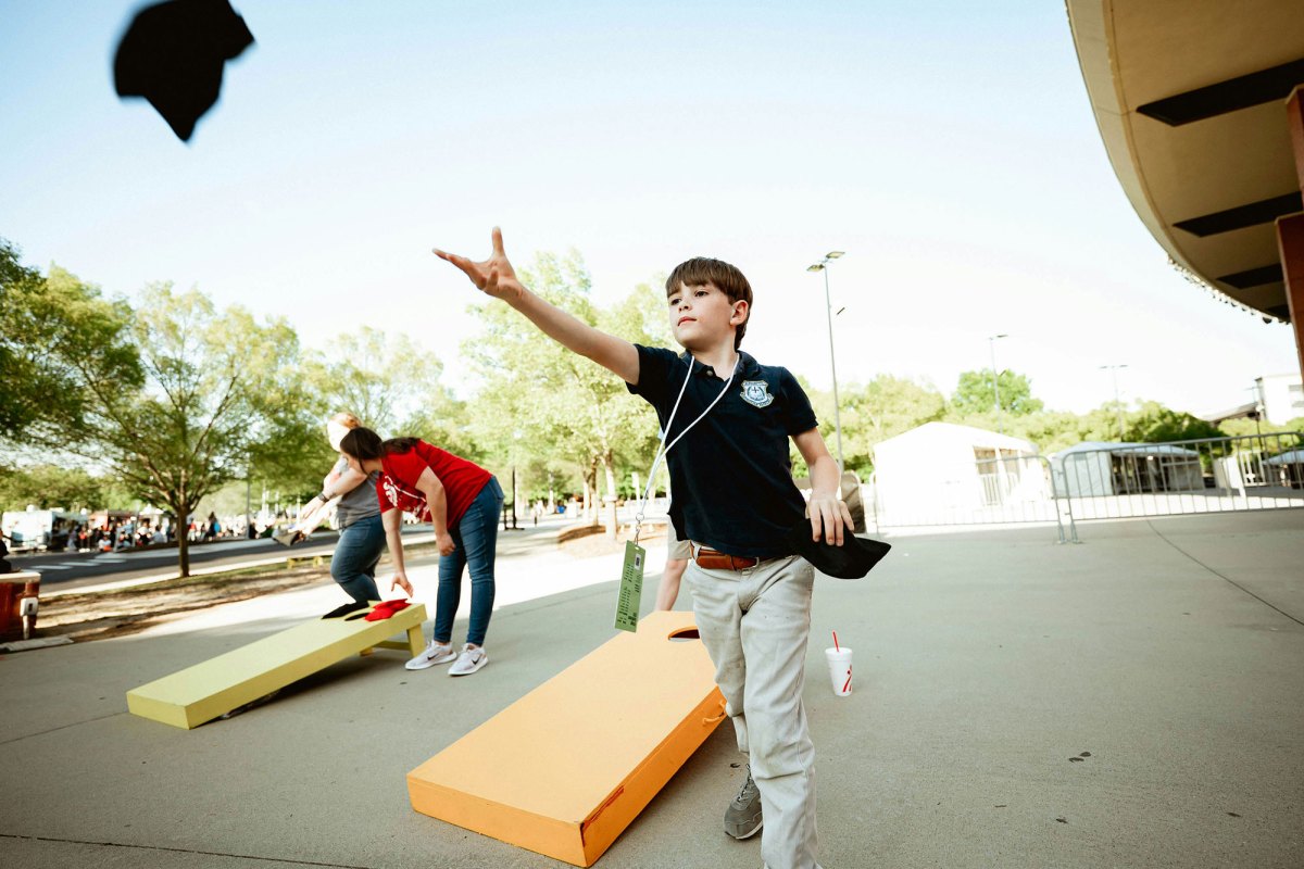 A boy playing corn hole wearing a black shirt and khaki pants