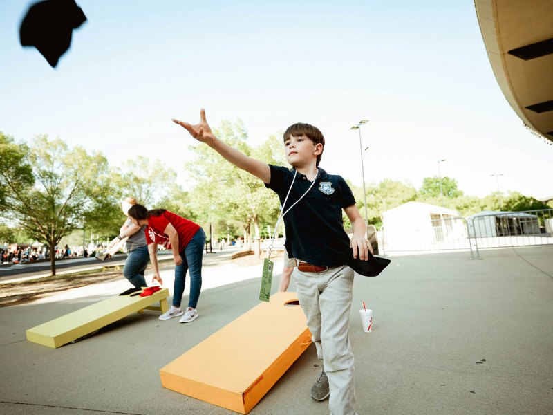 A boy playing corn hole wearing a black shirt and khaki pants