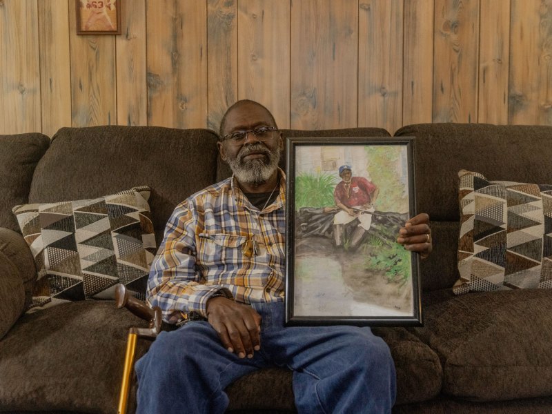 A man sitting on a brown couch holding a photo of himself
