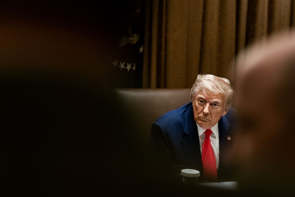 A view of Donald Trump seen in the background between people who are seen out of focus