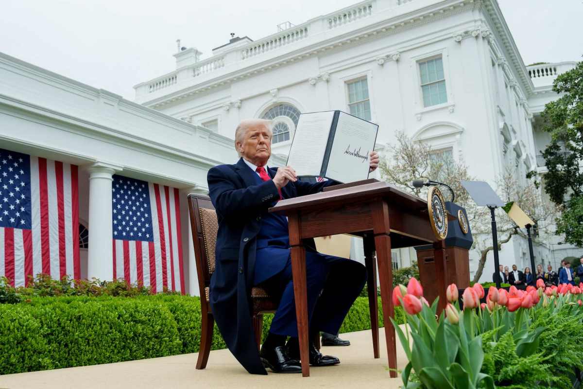 a photo of donald trump sitting at a desk in the Rose Garden outside holding up a signed executive order