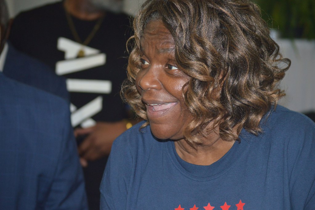 A woman with black and brown hair smiles big in the photo wearing blue shirt with red stars on it.