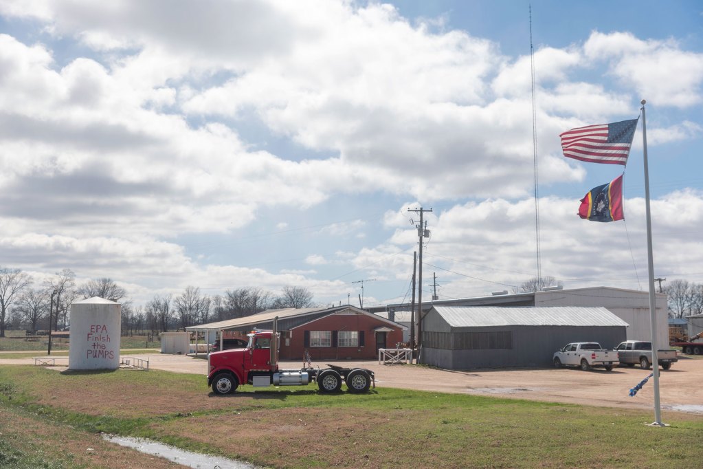 A red truck sits in green grass with flags to the right of it and a blue sky in the background
