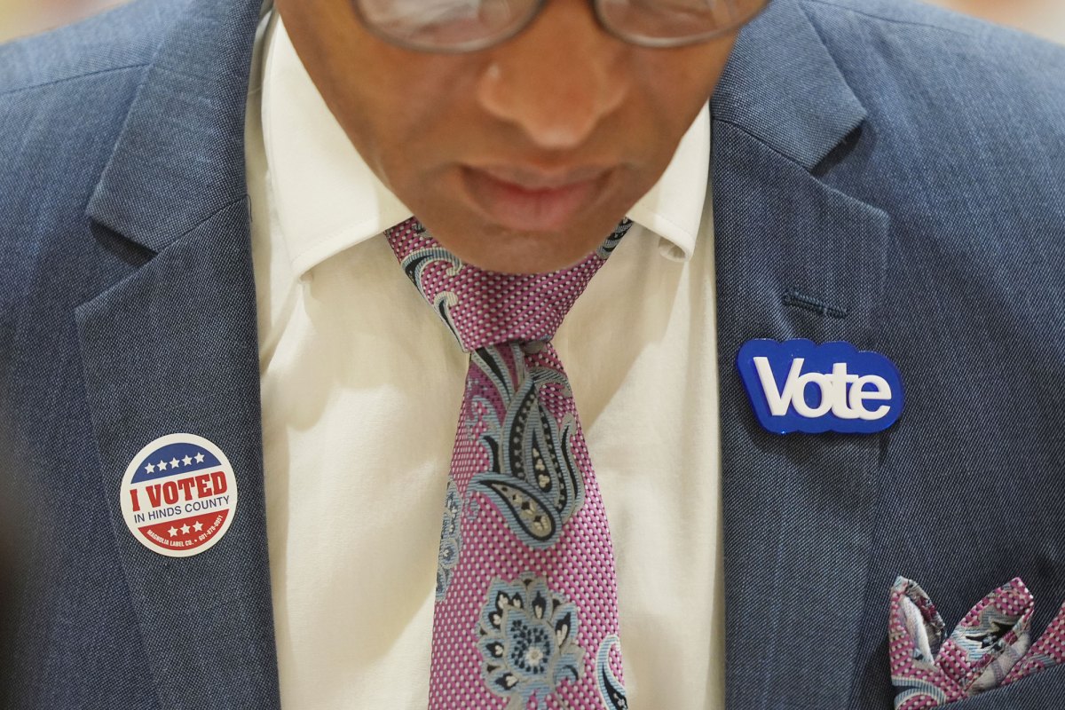 Closeup of a person in a suit's chest, showing an I Voted in Hinds County sticker on the left lapel, and a Vote pin in the right.