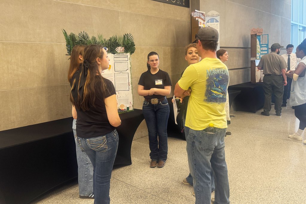 Girl stands in front of trifold board talking to three adults