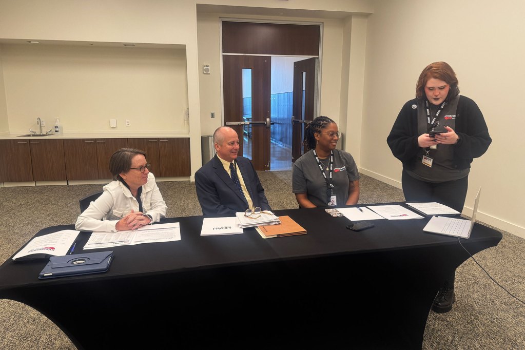 Adult male, adult female and female student sitting at table with adult standing using phone