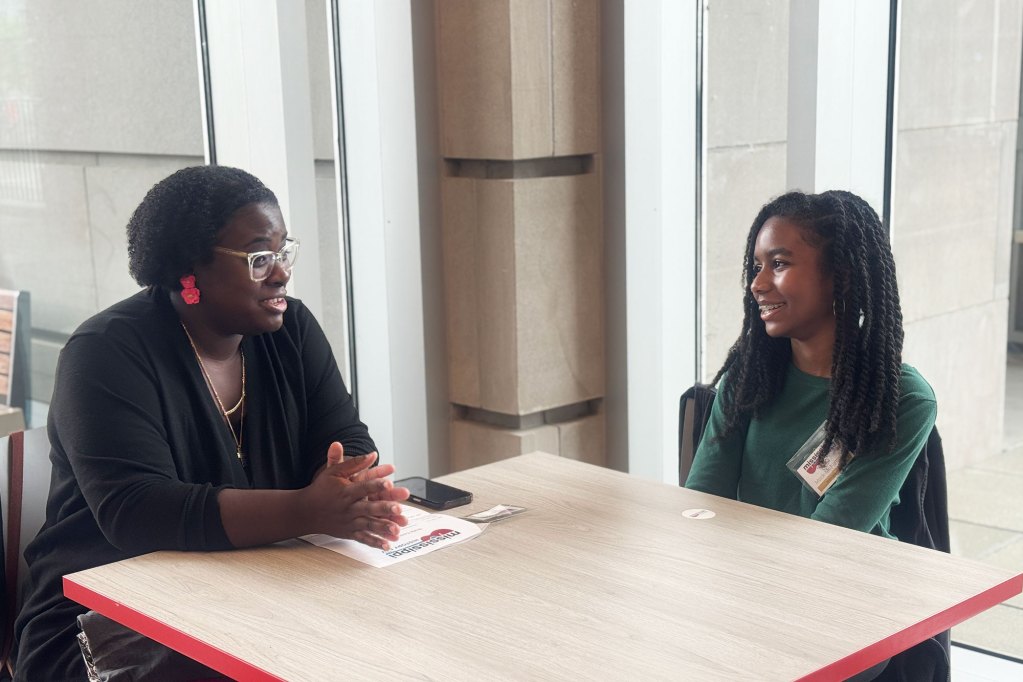 Adult teacher sitting at table with student, talking together