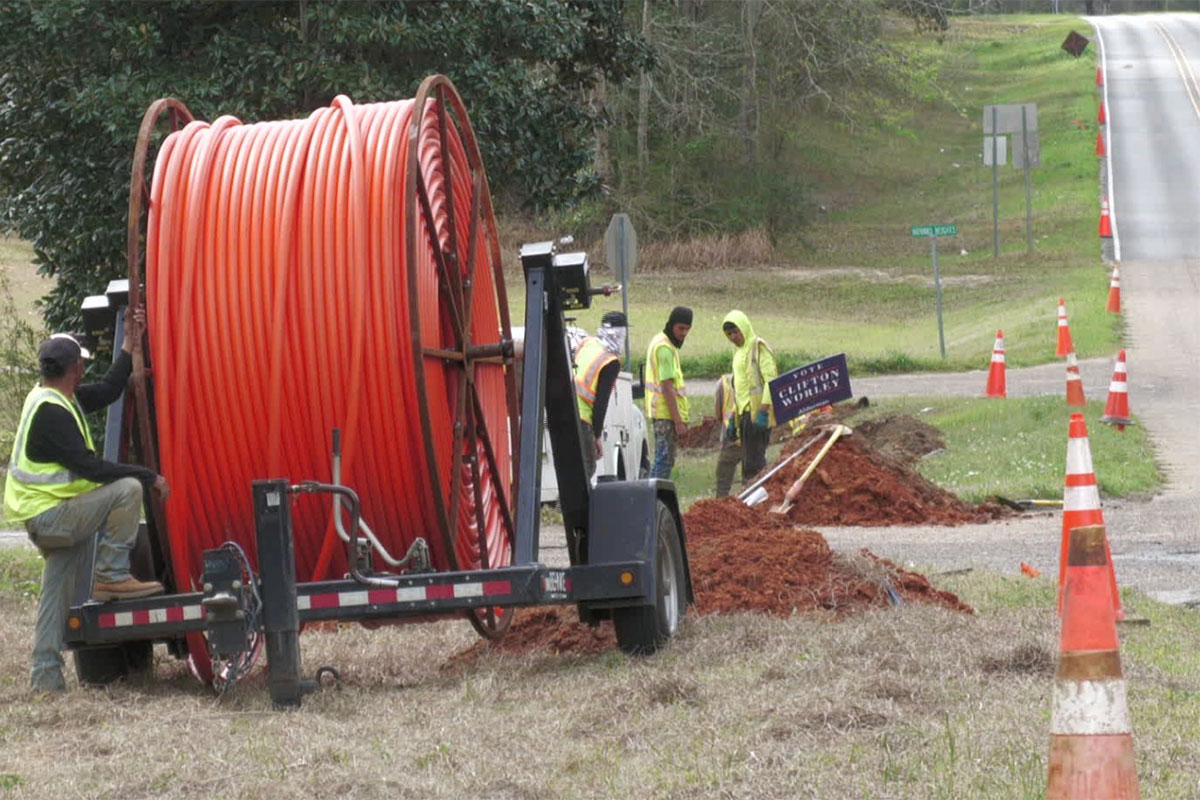 A crew in high visibility vests work with a giant orange spool of cable