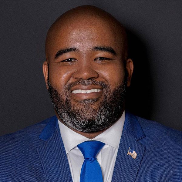 Closeup of a bearded man with a US flag pin on the lapel of his blue suit