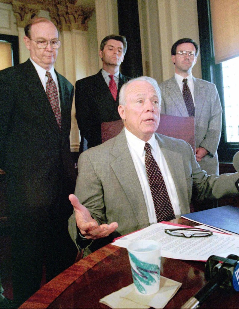Kirk Fordice sitting at a desk with three other white men behind him