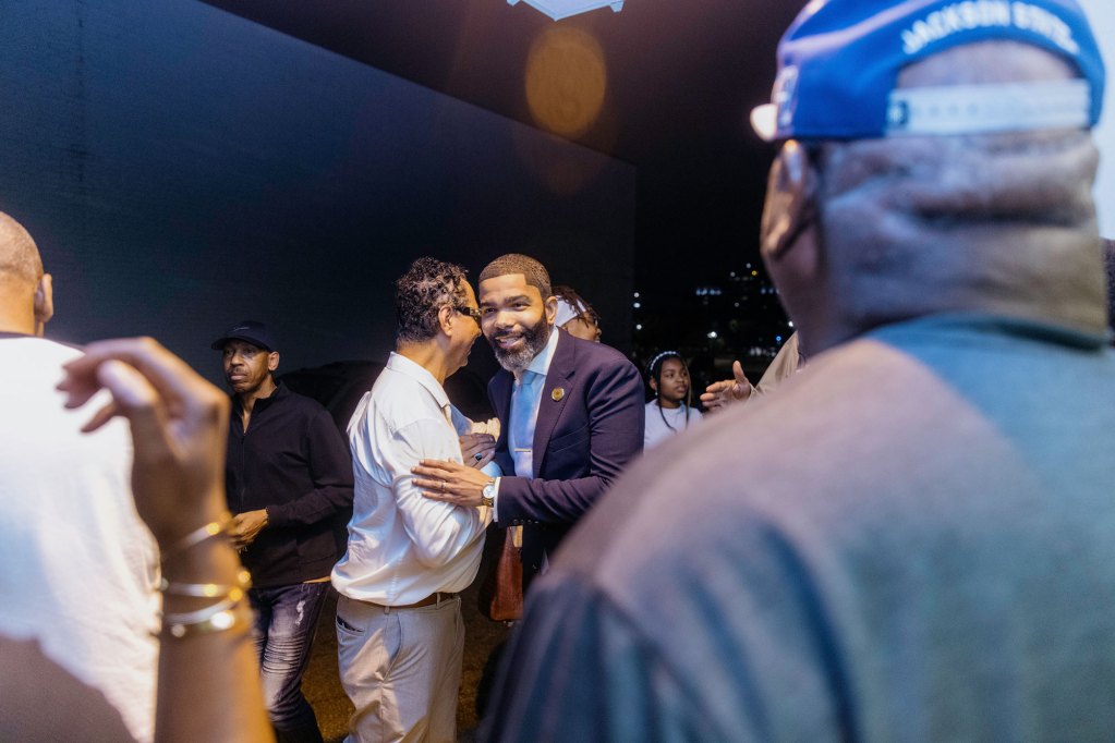 Chokwe A. Lumumba in a blue suit shaking the hand of a man in white shirt and tan pants