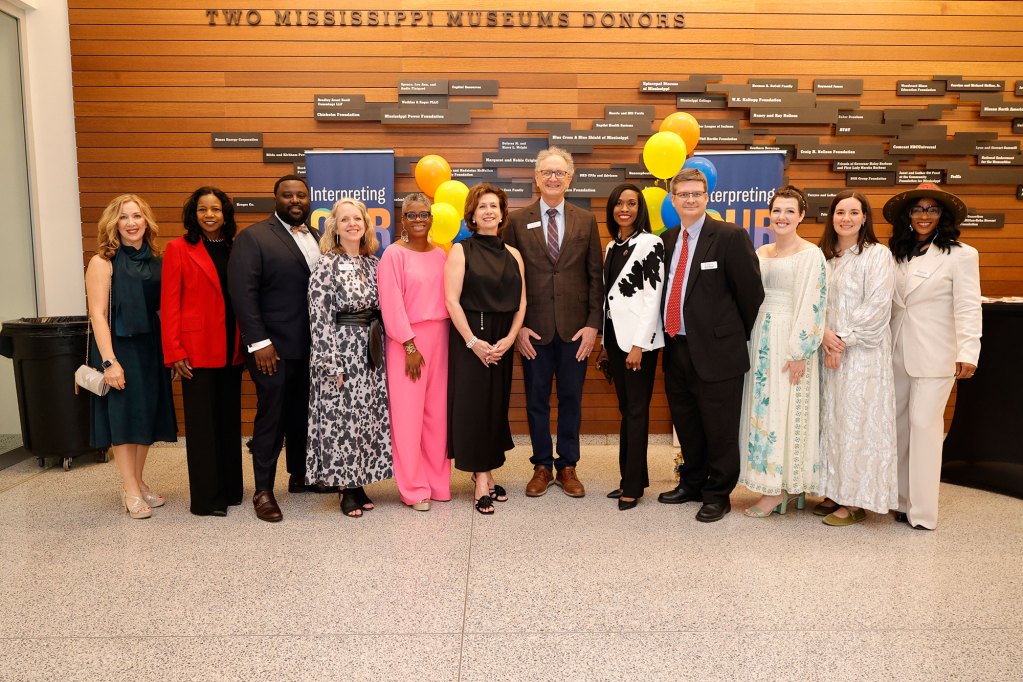 A group of men and women standing in front of yellow, orange, and blue balloons