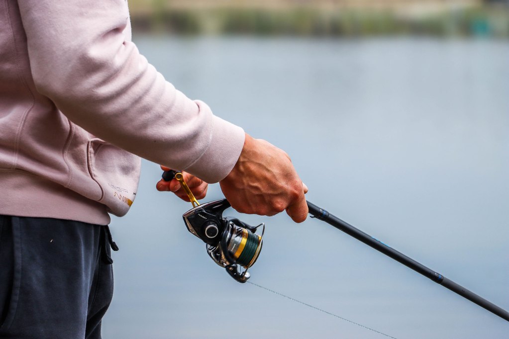 A man in a pink sweatshirt and blue pants holds a fishing rod