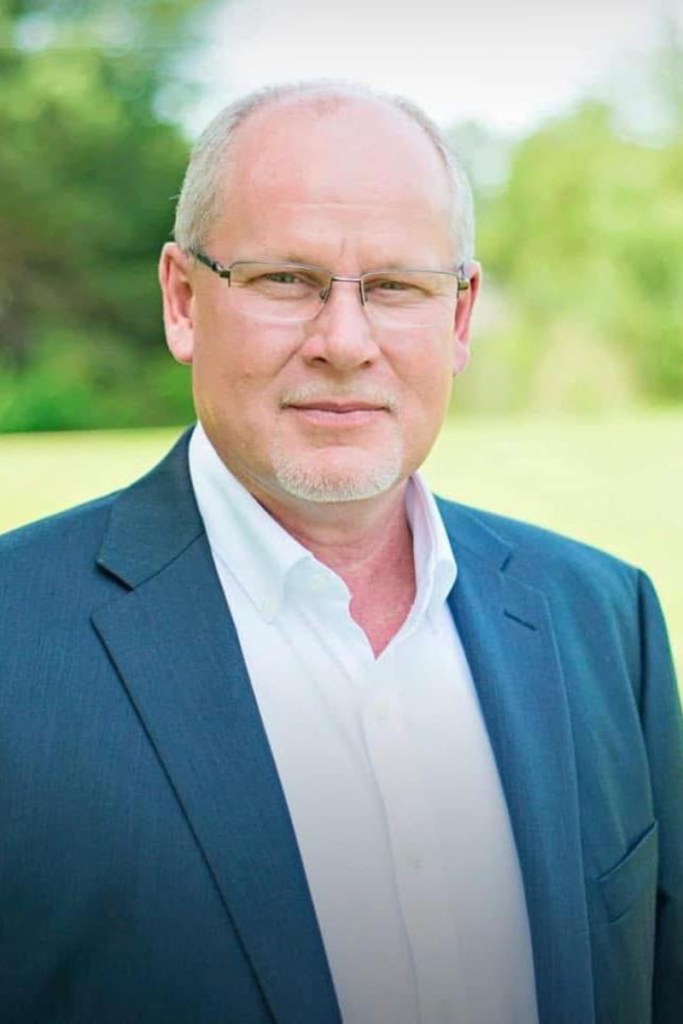 A man wearing a blue jacket and glasses poses outside