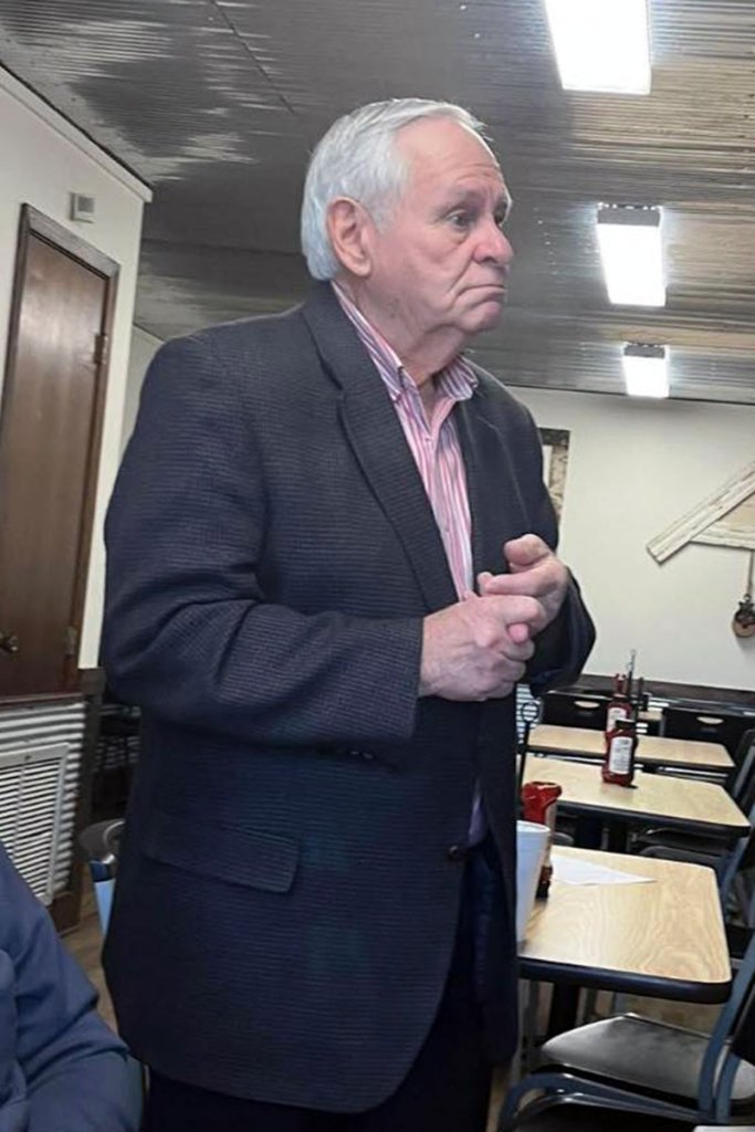 An older man in a suit stands up inside a restaurant