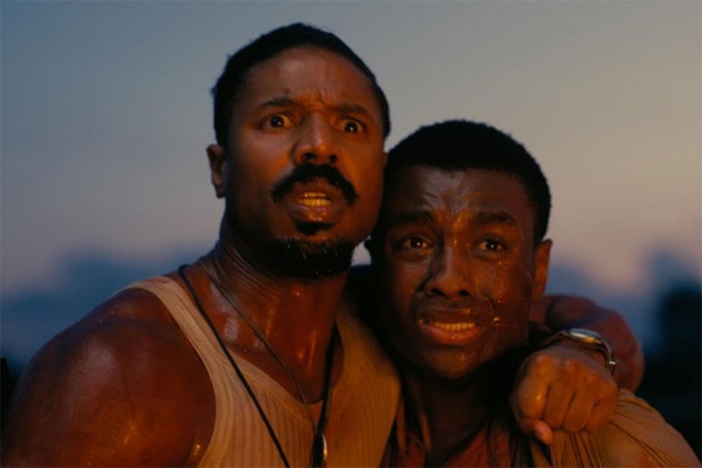 Two men hold each other close and look at something, crying