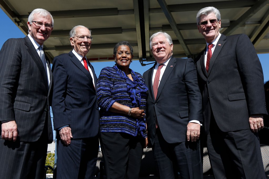 Four men and one woman stand together on an outdoor stage