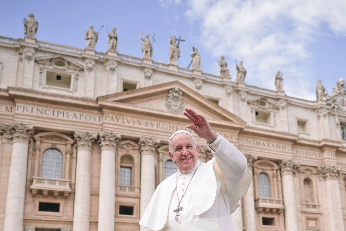 Pope Francis, in white, smiles and waves from in front of a Vatican building