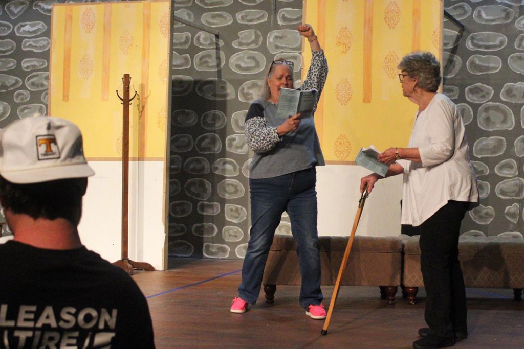Three people stand on a theater stage during practice