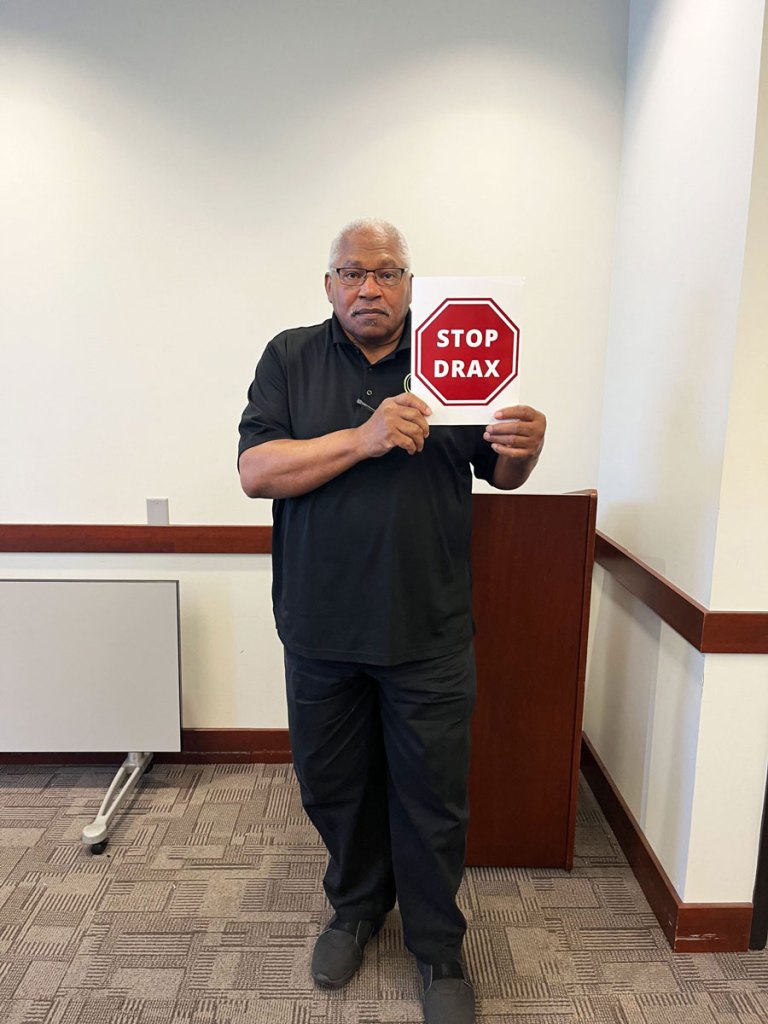 A man wearing black holds a Stop Drax sigh in his hand