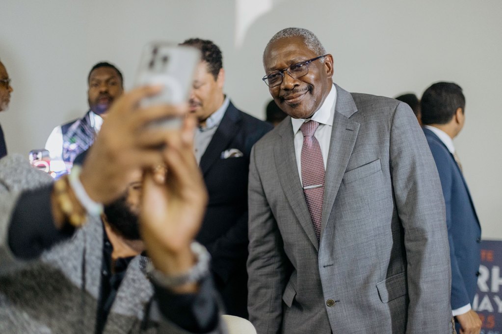 John Hohrn in a suit watching as someone's arm is reached out holding a cell phone to take a photo