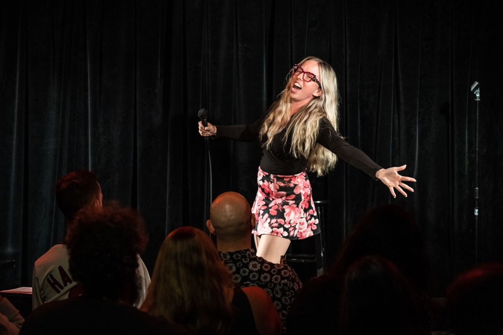 A woman performing in front a crowd wearing a black shirt and a floral print skirt.