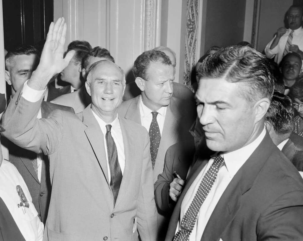 an old black and white photo of a man in a suit waving at the camera while other men in suits surround him