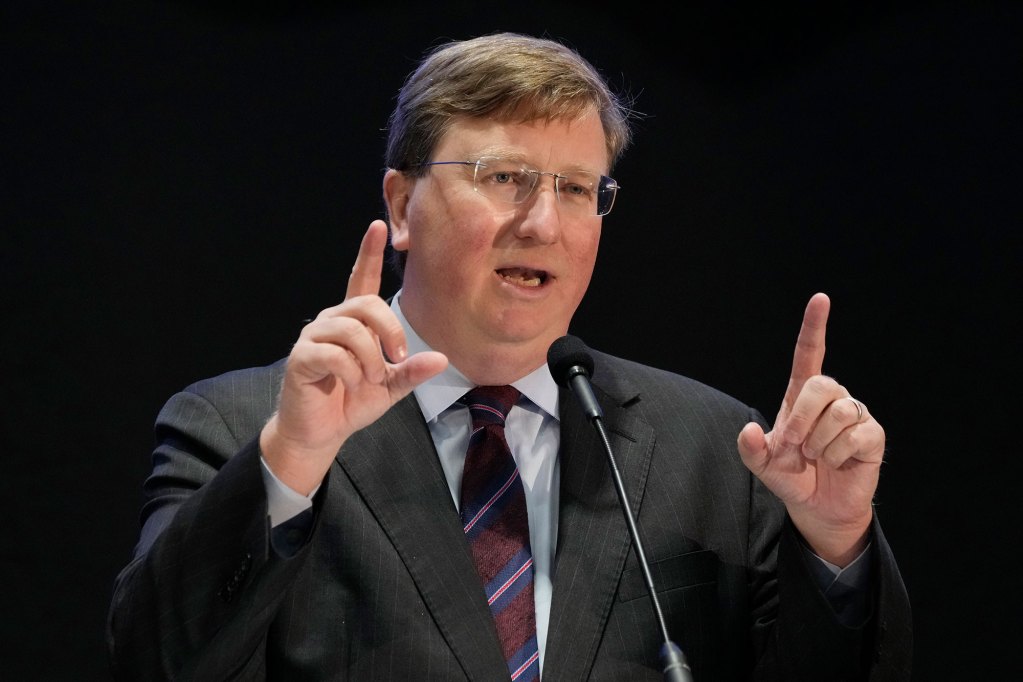 Tate Reeves speaking at a mic with both hands pointing in the air