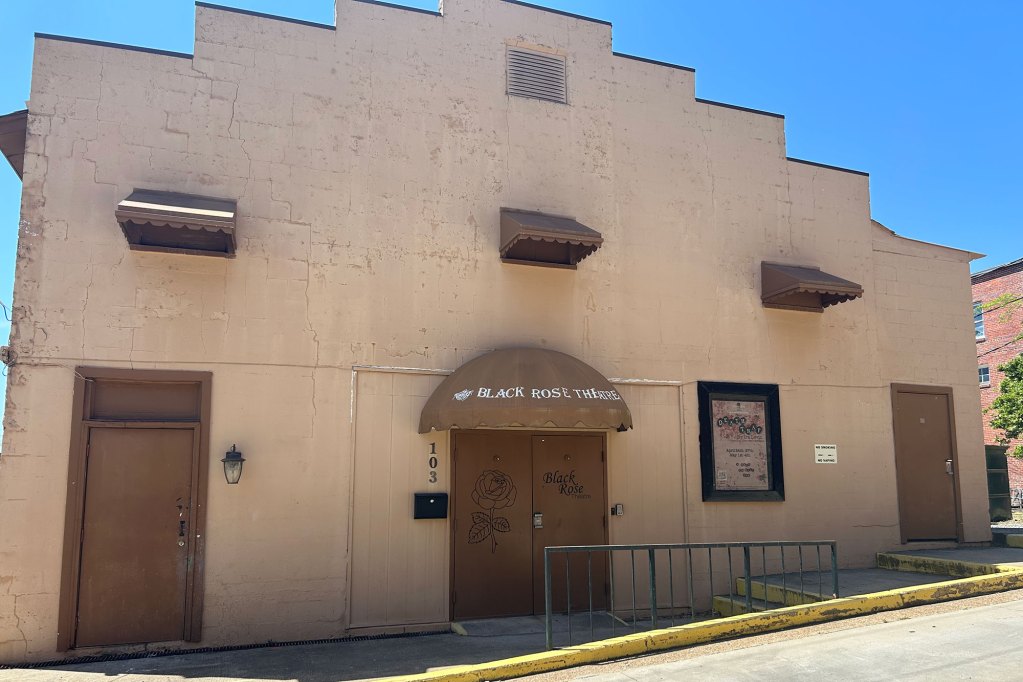 A beige exterior of a building with a geometric step-like roof and a sign that reads Black Rose Theatre