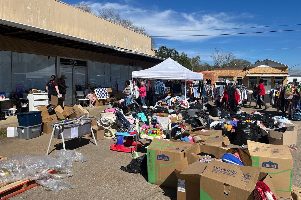 Men and women surrounded by boxes of clothes in the parking lot of a business.