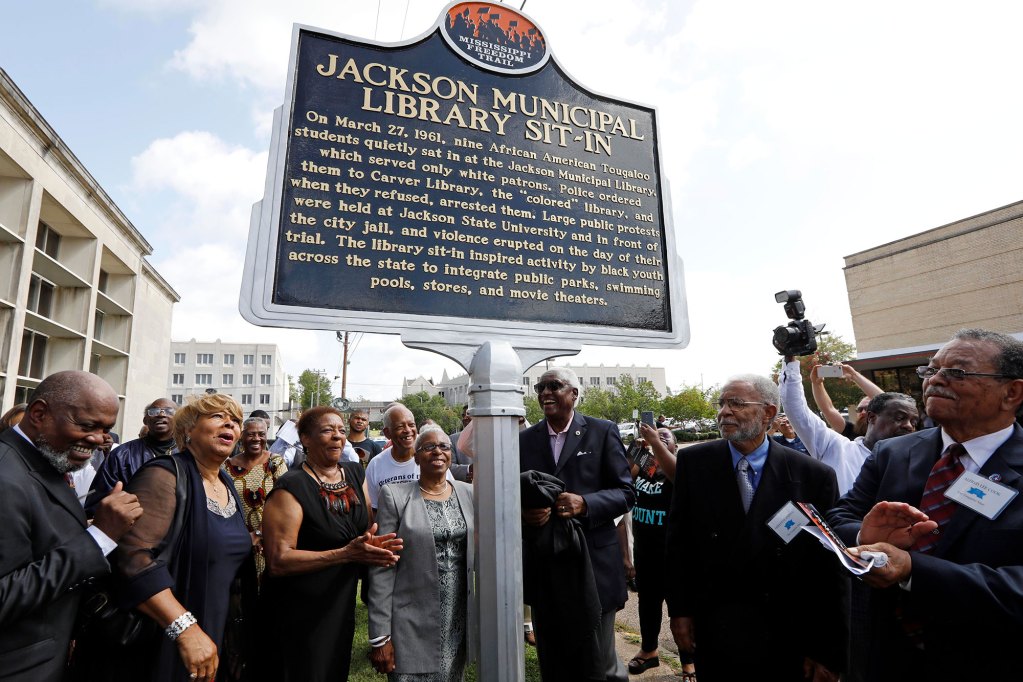 A crowd of people look on and clap to a new historical marker. The title on the marker is Jackson Municipal Library Sit-In