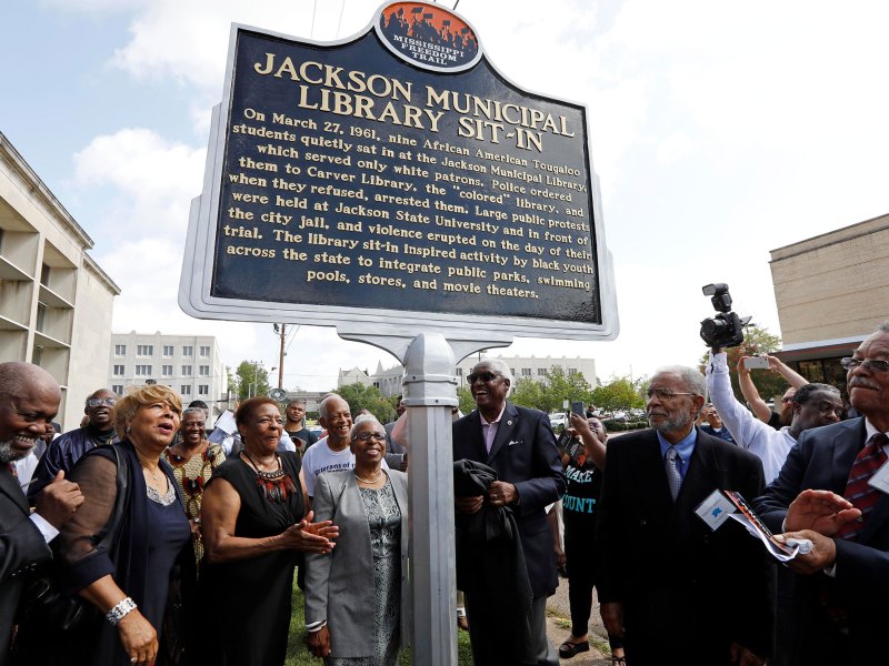 A crowd of people look on and clap to a new historical marker. The title on the marker is Jackson Municipal Library Sit-In