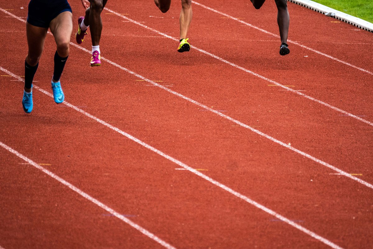 In this photo are legs of track runners on an orange and white track field