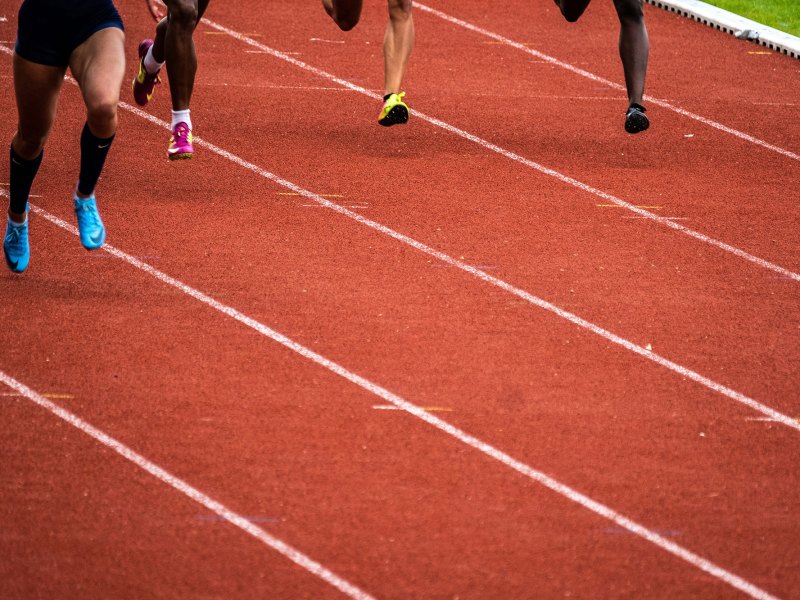 In this photo are legs of track runners on an orange and white track field