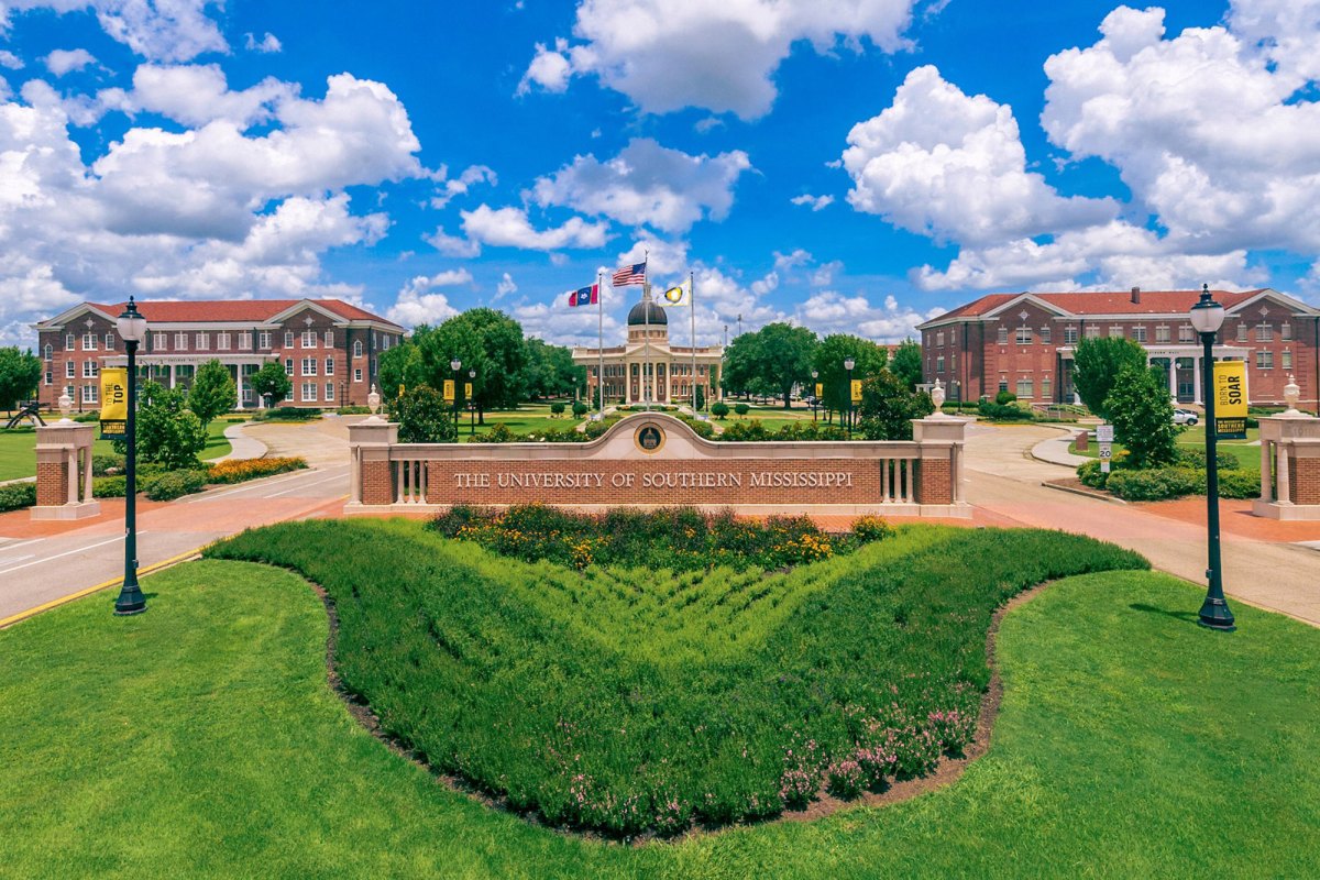 The University of Southern Mississippi front campus with green grass in the foreground and a blue sky in the background