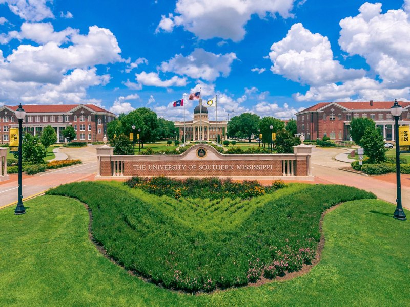 The University of Southern Mississippi front campus with green grass in the foreground and a blue sky in the background