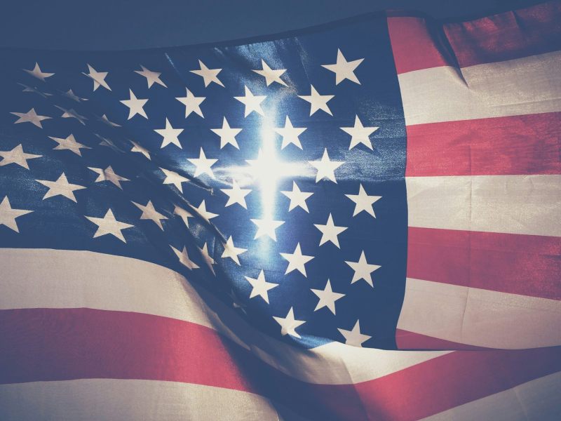 A US Flag waving, a cross like light shining through from the other side