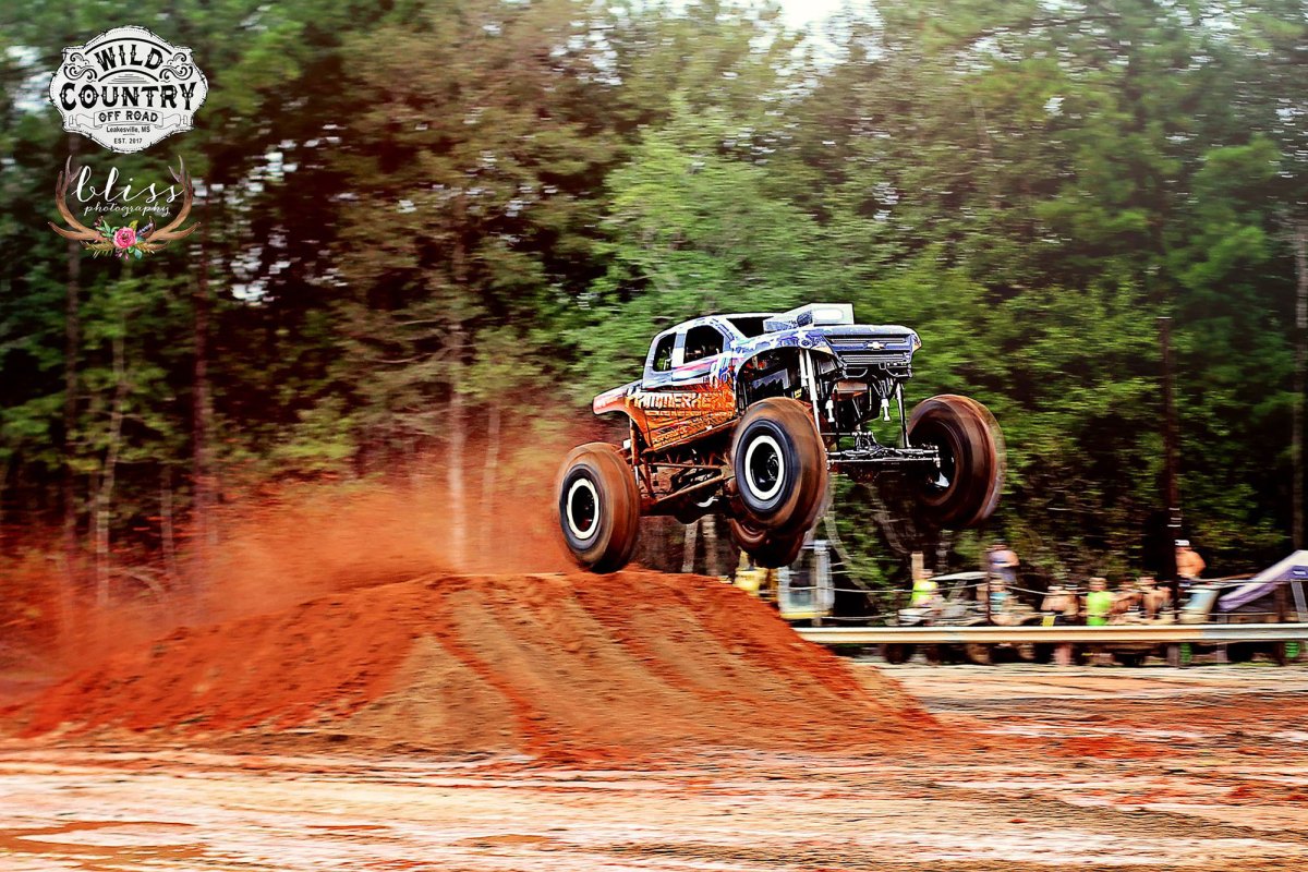 A mega truck performs a jump off of a large dirt ramp