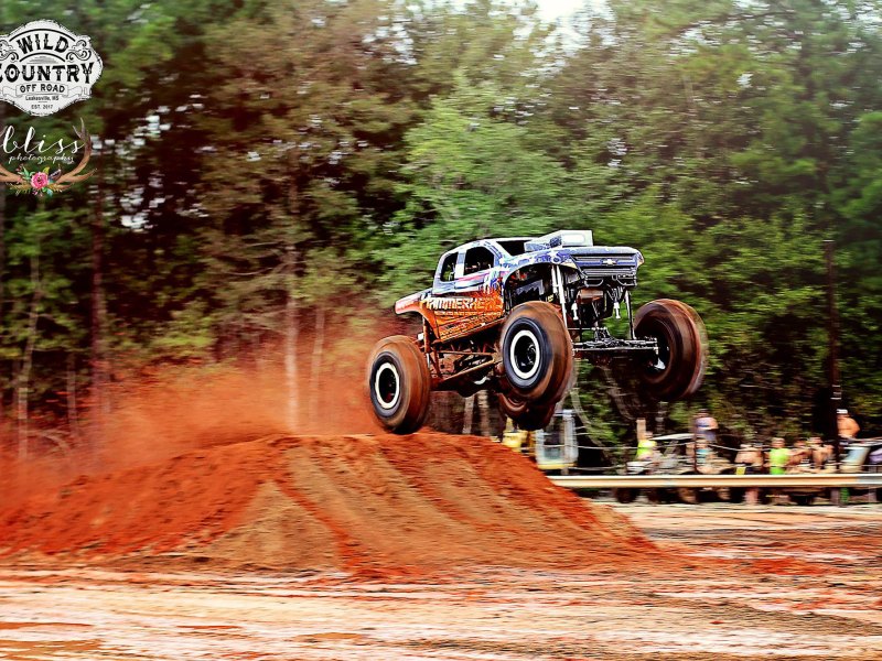 A mega truck performs a jump off of a large dirt ramp